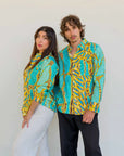 Male and female models wearing matching Kirrikin unisex Karijini long-sleeve shirts featuring vibrant turquoise and yellow Indigenous artwork by Sally White.