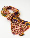 Kirrikin Stories In The Sun Luxury Cashmere Scarf styled in a loose knot on a white background, featuring red, yellow, and blue Indigenous circle artwork by Kaye White with frayed edges.