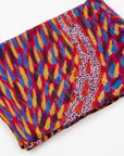 Folded Storms in the Pilbara Silk Chiffon Scarf by Kaye White, displaying vibrant red, yellow, and blue Indigenous artwork patterns.