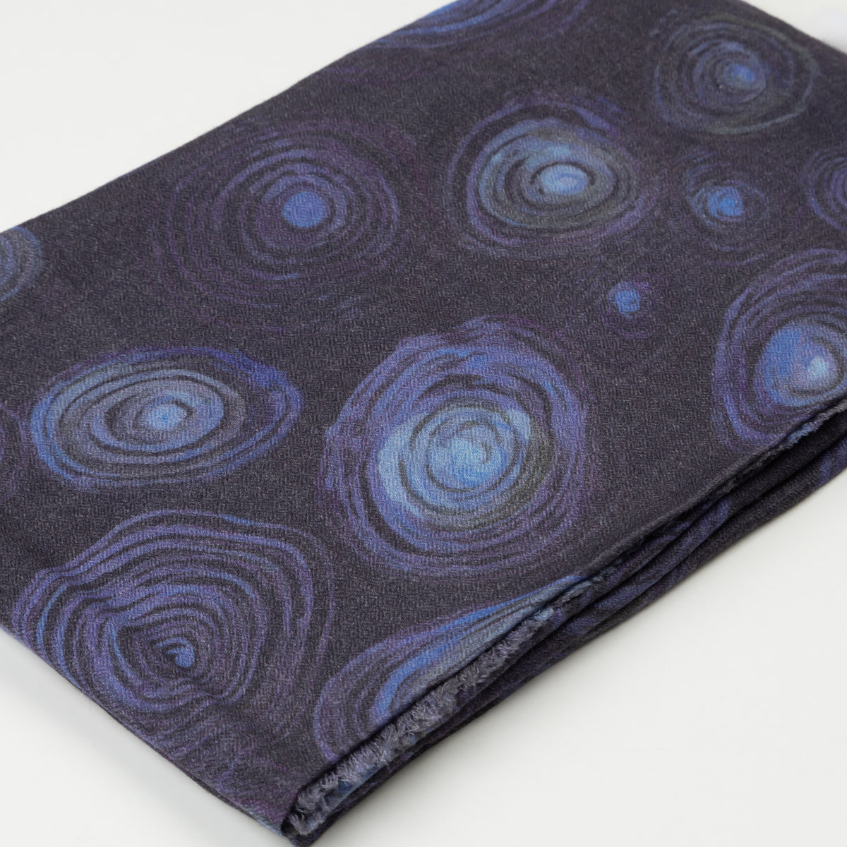 Close-up of folded 100% Cashmere Scarf displaying the detailed deep blue and purple concentric circle pattern designed by artist Helena Geiger.
