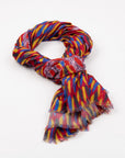 Kirrikin Storms In The Pilbara Luxury Cashmere Scarf styled in a loose knot on a white background, featuring red, yellow, and blue Indigenous artwork patterns with naturally frayed edges.